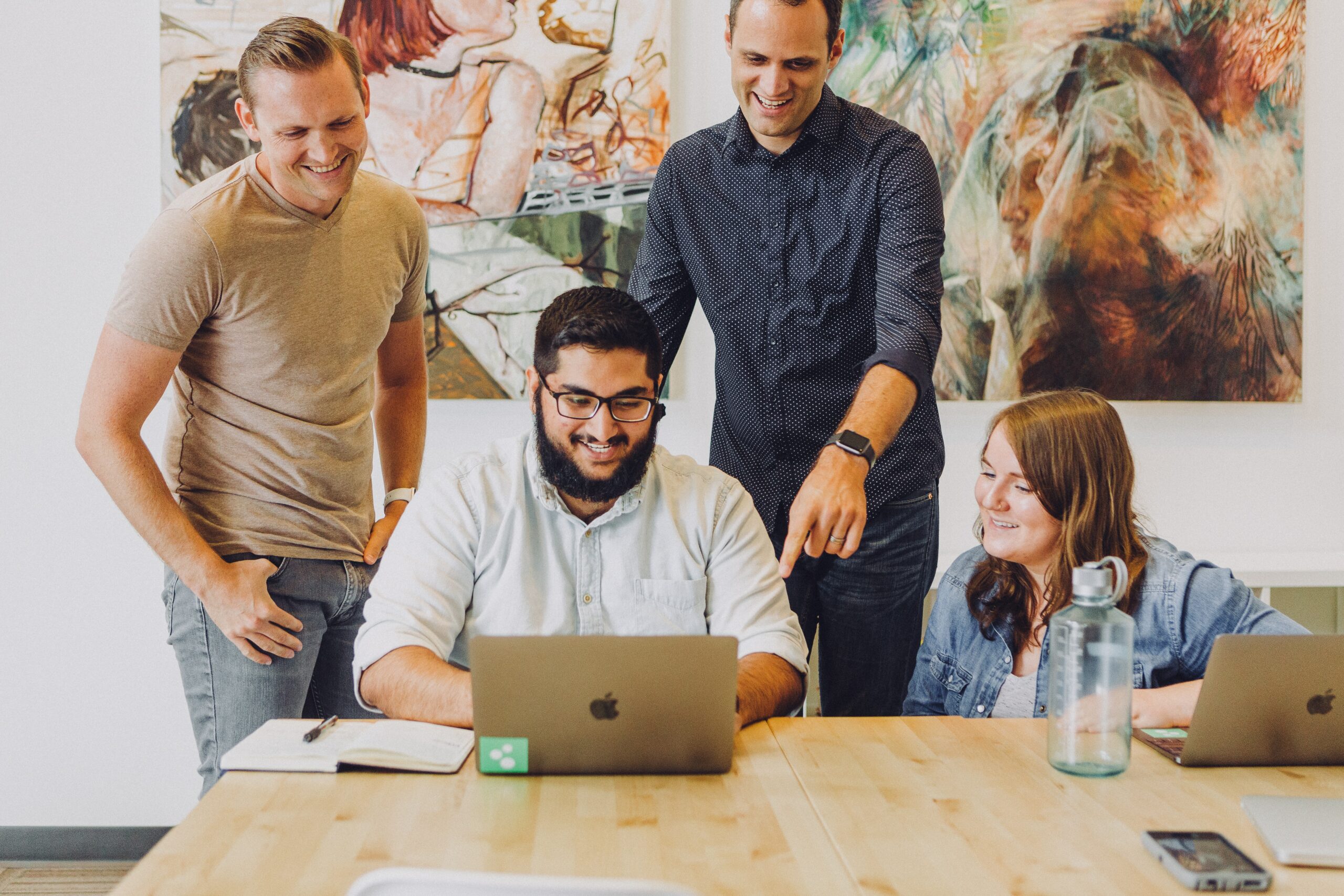 Group of colleagues sat around a table with a laptop smiling